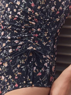Zwart met broderie en fijne print - Badpak met vormgevende zijrimpeling en buikcorrectie