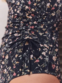 Zwart met broderie en fijne print - Badpak met vormgevende zijrimpeling en buikcorrectie